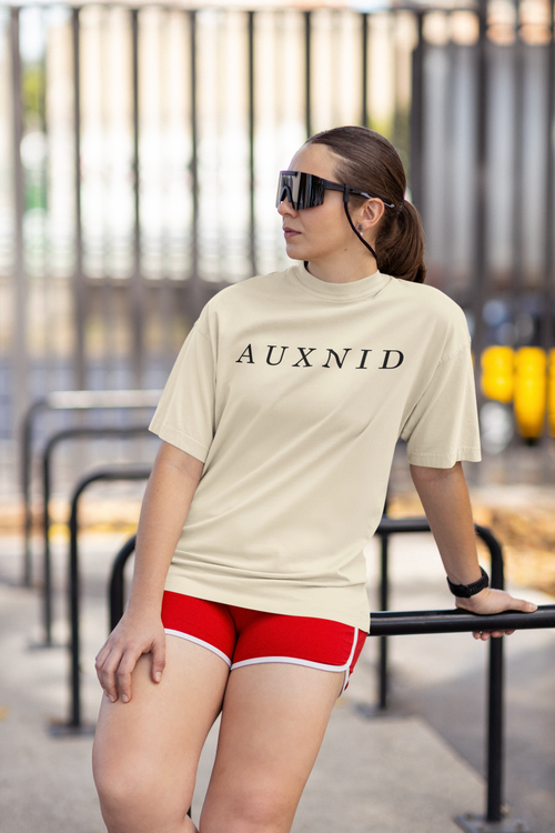 Woman wearing a beige 'AUXNID' t-shirt and red shorts, standing outdoors.