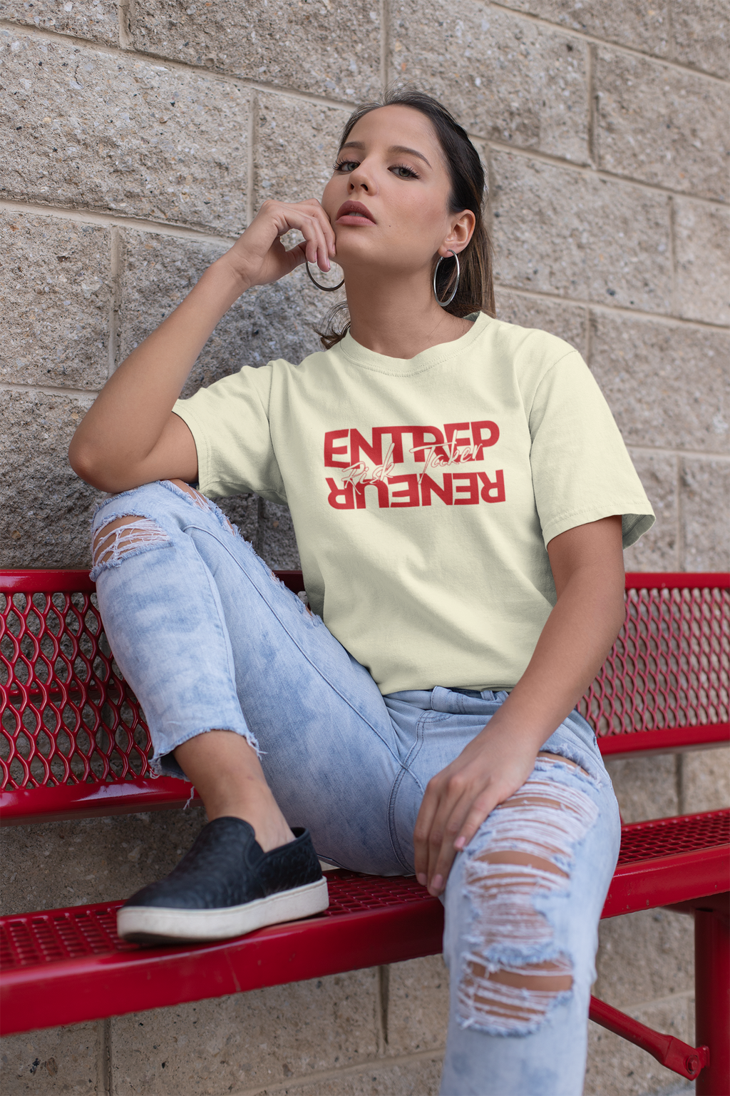 Woman sitting on a red bench wearing a light green t-shirt with red text and light blue jeans.
