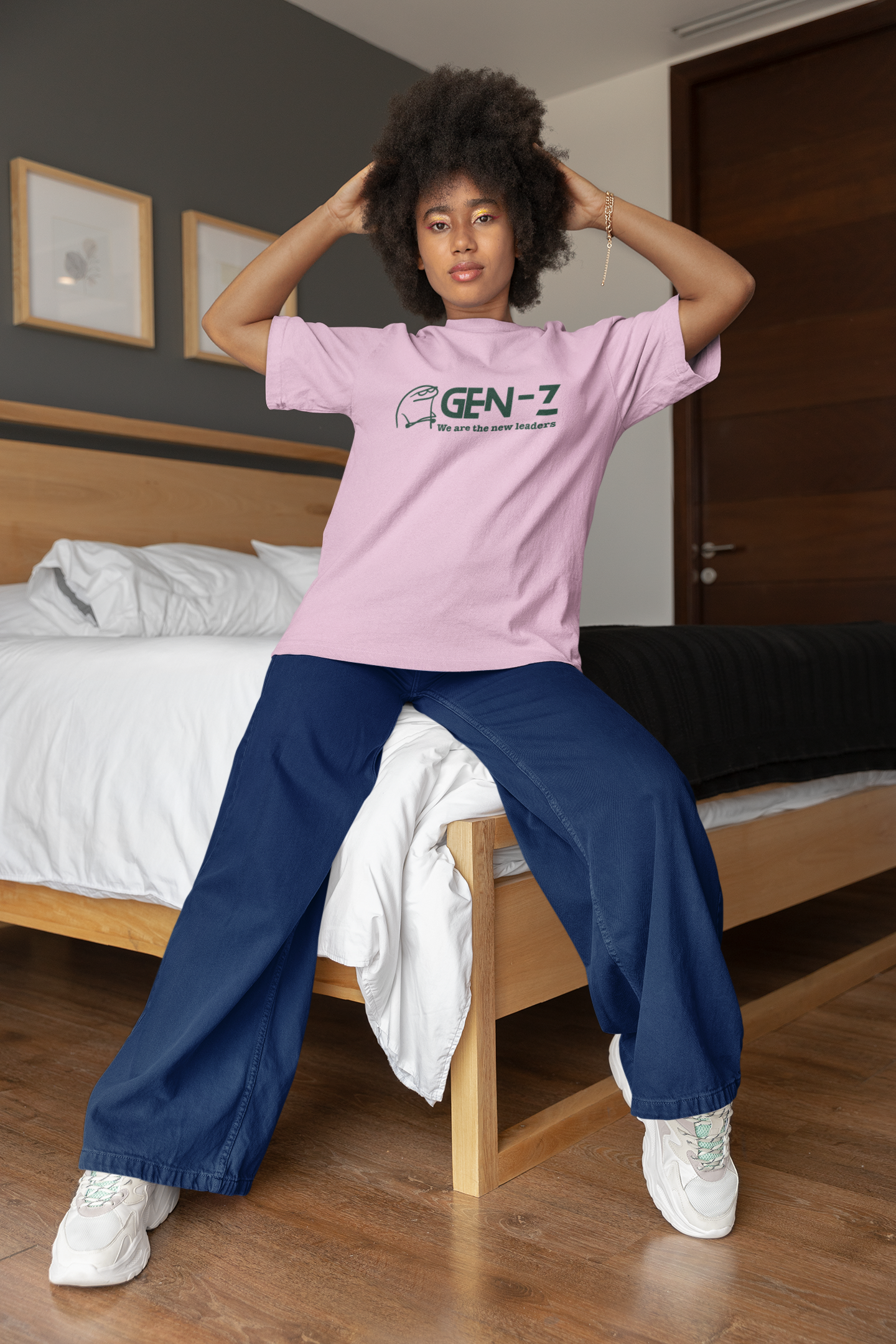 Person wearing a pink 'GEN-Z' t-shirt sitting on a bed in a bedroom.