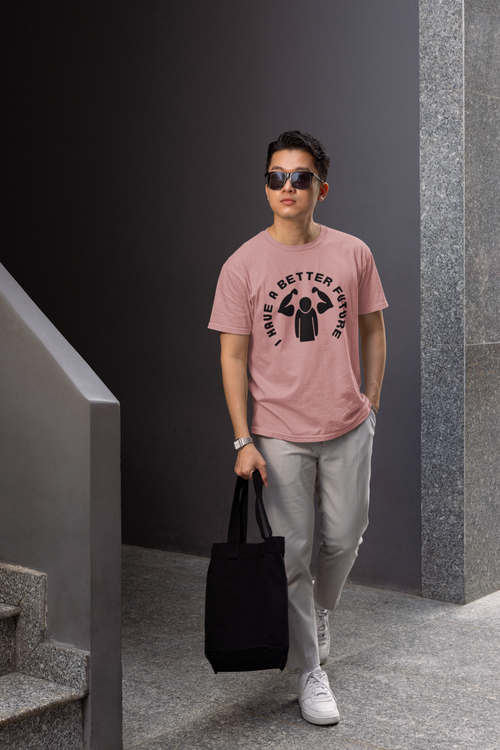 Man wearing a pink t-shirt with a graphic design, holding a black tote bag, standing against a dark wall.