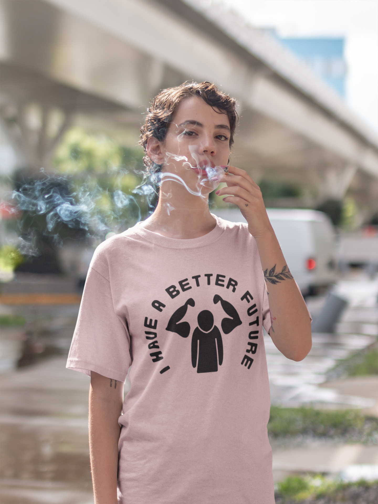 Person wearing a pink t-shirt with a graphic and text, smoking a cigarette outdoors.