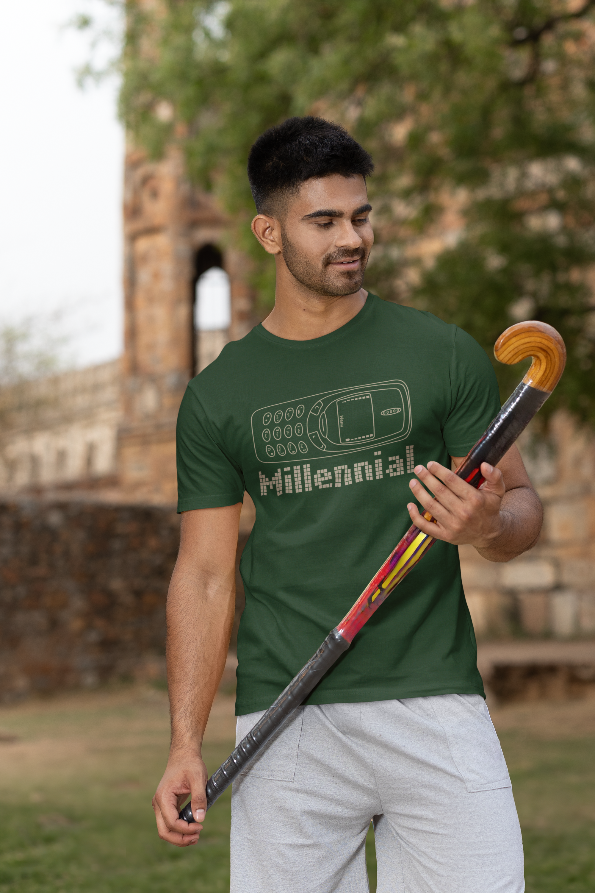 Man wearing a green t-shirt with 'Millennial' design, holding a hockey stick outdoors.