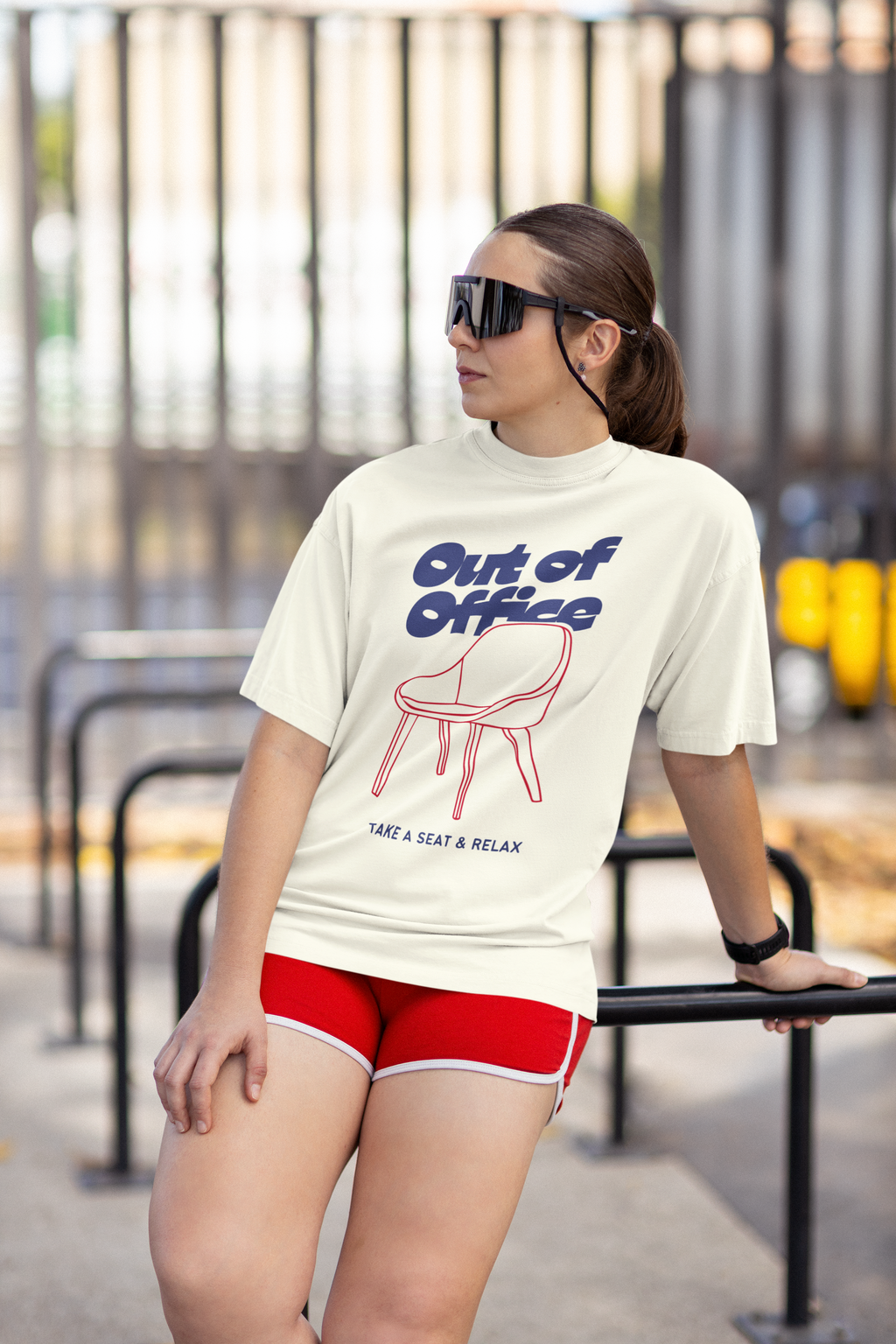Woman wearing a white t-shirt with 'Out of Office' text and red shorts, standing outdoors.