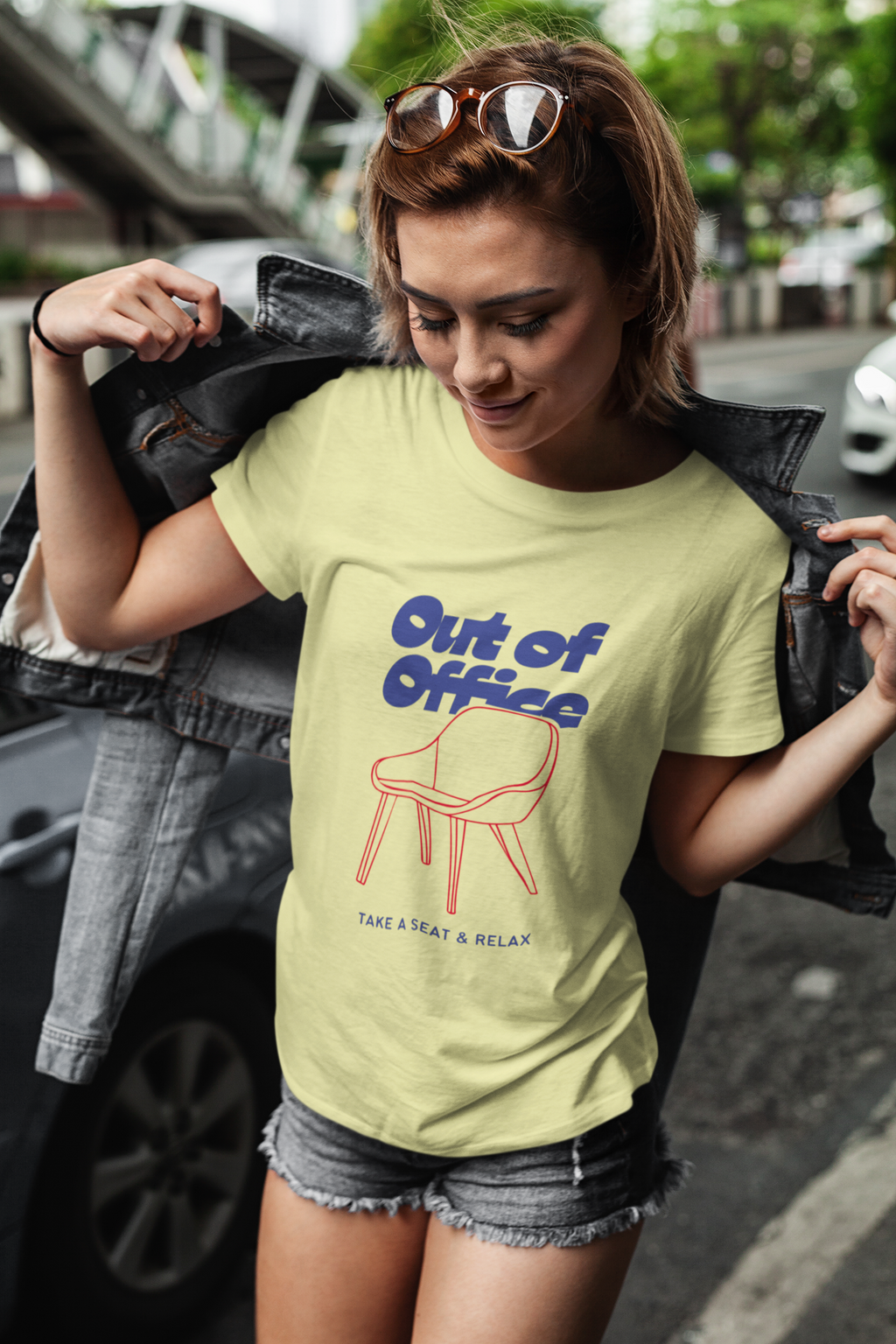 Woman wearing a light green t-shirt with 'Out of Office' text and chair graphic, standing outdoors.