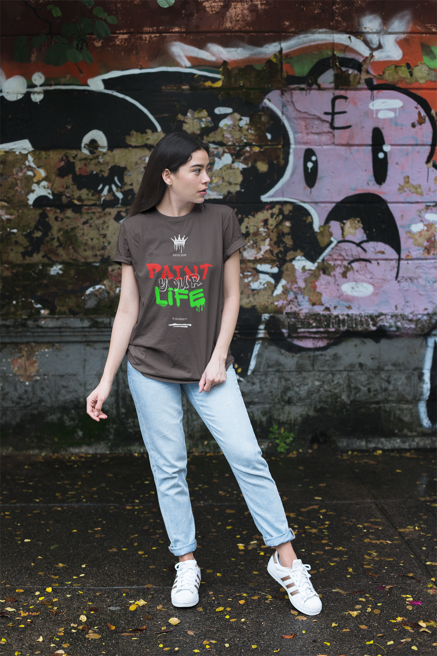 Person wearing a brown t-shirt with text standing in front of a graffiti-covered wall.