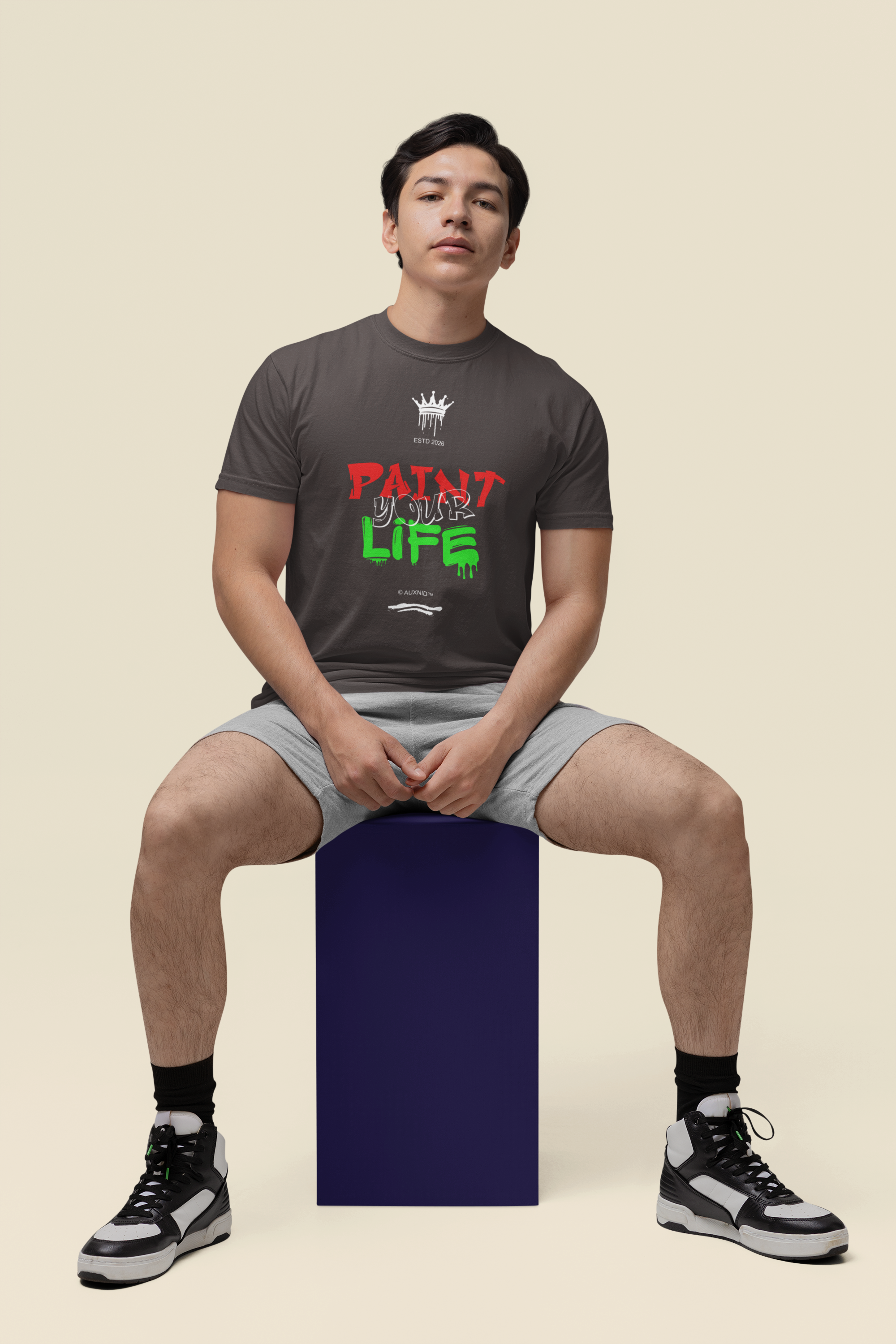 Person sitting on a purple block wearing a dark t-shirt with colorful text and graphics.